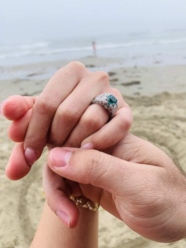 Couple holding hands showcasing custom emerald engagement ring by Kaz Jewelry in Laguna Niguel